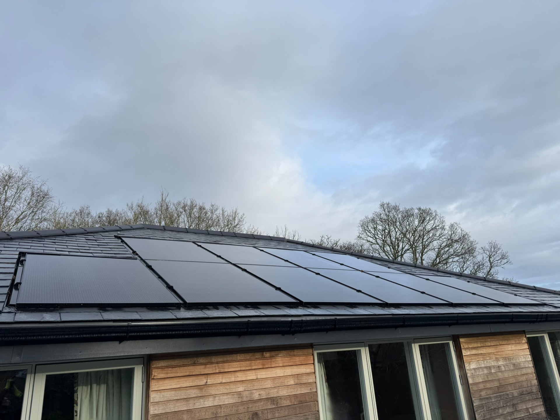 Clean black solar panels on a slate roof above a timber-clad home near Lymington
